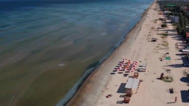 Yazın sahilde güzel bir uçuş. İnsanlar deniz kenarında dinleniyor. Turistler için evler. Plaj şemsiyeleri, gezintiler, denizde yüzen insanlar..