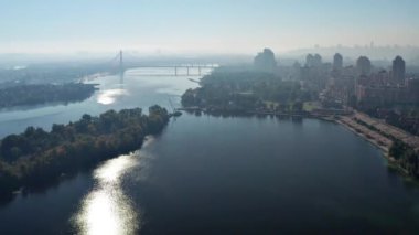 Kyiv ve Dinyeper Nehri üzerinde güzel bir uçuş. Güneş nehire yansıyor. Arka planda nehir boyunca sis ve köprü var. Dinyeper seti boyunca çok katlı binalar..