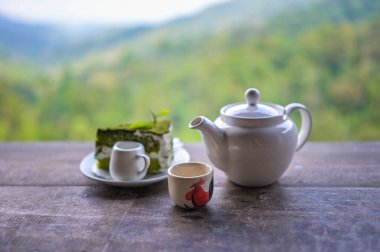 Çay takımı, fincanlar ve çaydanlık yeşil çaydanlık, dağ ve orman arka planına sahip ahşap tahtada..