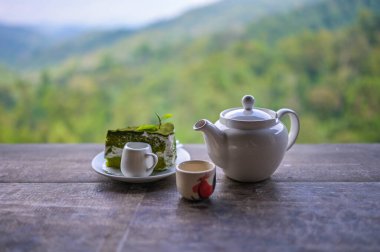 Çay takımı, fincanlar ve çaydanlık yeşil çaydanlık, dağ ve orman arka planına sahip ahşap tahtada..