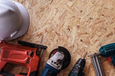 Group of electric hand tools jigsaw, grinder, drill, nail gun and white safety helmet on wooden background.