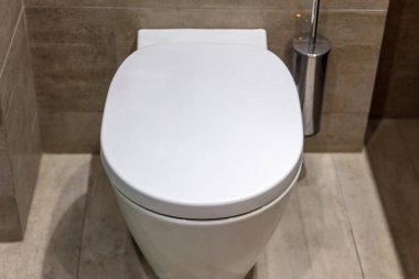 Modern tuvalet tasarımı, kapalı kapaklı ve fırçalı beyaz klozet asmak. Lüks banyo aksesuarları mermer kaplama duvarlar ve zemin açık gri arka plan.