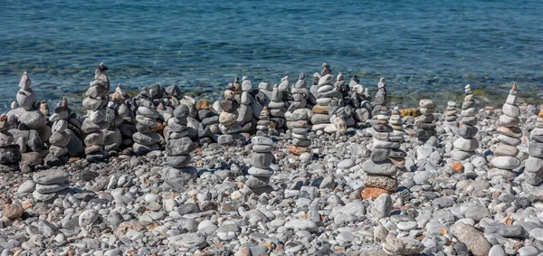 Zen stones, rock pyramids stacked on pebble beach, blue sea background, sunny day. Children or family creativity on the seashore, summer vacations