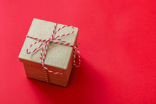 礼品盒 圣诞红白色条纹丝带蝴蝶结 棕色牛皮纸节日礼物 红色背景 顶视图 自制迪米生态包装材料 — 图库照片