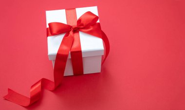 Kırmızı arka planda kurdeleli Noel beyaz hediye paketi, sevgililer günü sürprizi, yeni yıl hediyesi, saten kıvırcık süslemesi. Boşluğu kopyala, tebrik kartı şablonu