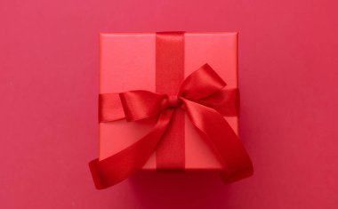 Kırmızı kurdeleli Noel hediyesi paketi kırmızı arka planda, kurdeleli, sevgililer günü sürprizi, yeni yıl hediyesi, saten kıvırcık süsleme, üst manzara.