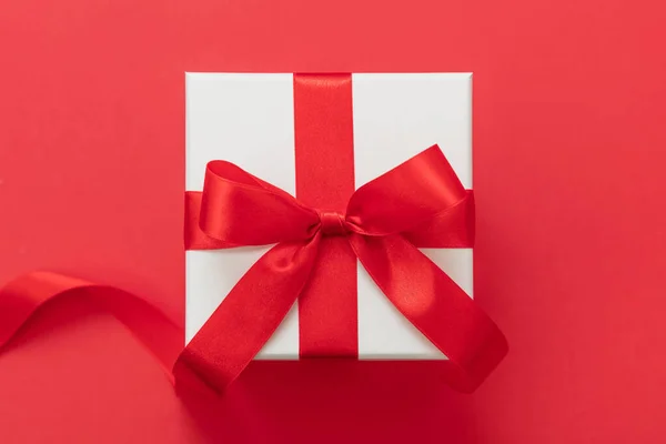 圣诞礼品盒白色 红丝带结蝴蝶结红色背景 情人节惊喜 新年礼物 缎子卷曲装饰 顶视图 — 图库照片