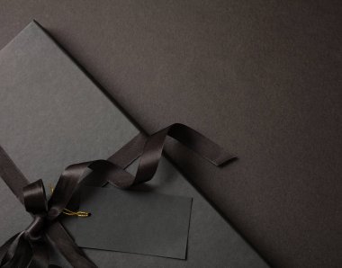 Kara Cuma indirimi konsepti, hediye kutusu detay kurdelesi yayı ve siyah arka planda boş etiket. Kış mevsiminde tatil promosyonu şablon, alan sunar