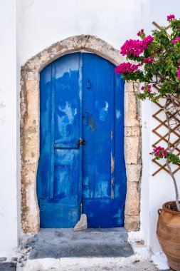 Tipik Yunan adası mimarisi. Kythira Chora kasabası, Yunanistan. Mavi ahşap kapı ve beyaz boyalı ev duvarında kırmızı begonvil. Güneşli yaz günü
