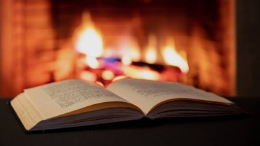 Kitap açık, şömine yanan odun arka planda. Ateşin yanında kitap okuyup rahatlamak, Noel tatili sıcacık bir ev.. 