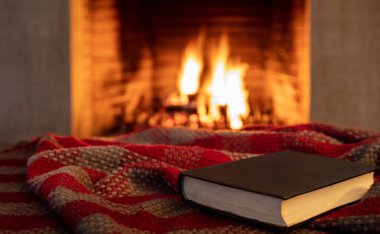 Battaniye üzerine kitap, şömine yanan odun arka planı. Ateşin yanında kitap okuyup rahatlamak, Noel tatili sıcacık bir ev.. 