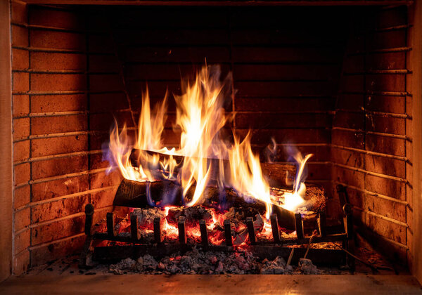 Fireplace burning firewood. Bonfire, fire flames on wood logs, bricks background. Cozy room interior at Christmas. Winter holidays relaxation and warm home