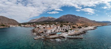 Yunanistan, Mora 'daki Mani yarımadasındaki Gerolimenas köyünün panoramik hava aracı görüntüsü. Geleneksel Lakonian mimarisi ve liman taşlı plajı şeffaf mavi turkuaz deniz bulutlu günü. Pankart