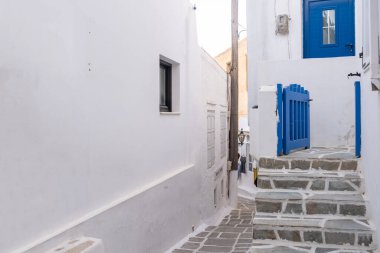 Beyazlatılmış binalar, taş döşeli merdivenler ve mavi ahşap çit girişi açık. Cyclades, Yunanistan. Ios, Nios Adası, Chora. Dar kaldırım taşı sokağı, geleneksel mimari