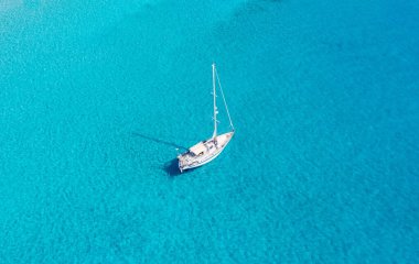 Yelkenli, sakin turkuaz deniz suyu arka planında demirli, hava aracı manzaralı. Yunanistan, Elafonisos Adası