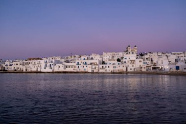 Paros Adası Yunanistan. Naoussa Köyü 'nün üzerinde gün batımı. Beyazlatılmış rıhtım binaları iskele üzerinde alacakaranlık, durgun deniz mavisi gökyüzü arka planı. Yaz hedefi.