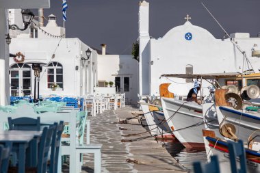 Greece, Paros island Naousa old port. Fishing boat moored at the harbor dock, cafe table and chairs outdoors at seaside.