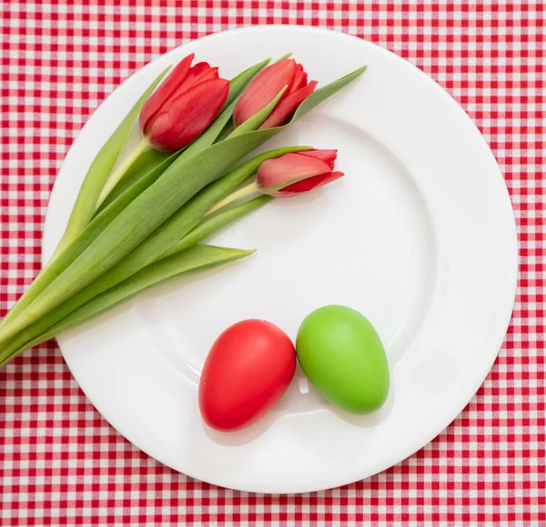 复活节假期桌上 白盘上的蛋 绿和郁金香装饰 格子桌布背景 顶视图 — 图库照片