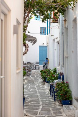 Naousa Yunanistan 'daki Paros Adası açık kafe tavernası. Kiklad mimarisi, dar kaldırım taşlı yaz gününde sandalyeye tahta masa yapan adam. Dikey