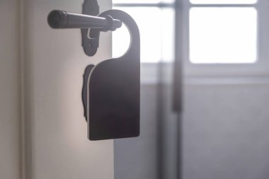 Otel odası askısı boş. Arka kapı tokmağında siyah etiket var. Yakın görüş. Beyaz ahşap kapı, bulanık oda içi