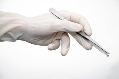 Forseps beyaz arka planda tek kullanımlık eldivenle doktor elinde. Hekimin elinde metalik, gümüş ve çelik cerrahi kıskaç var. Ameliyat için paslanmaz araçlardan oluşan tıbbi ekipmanlar.