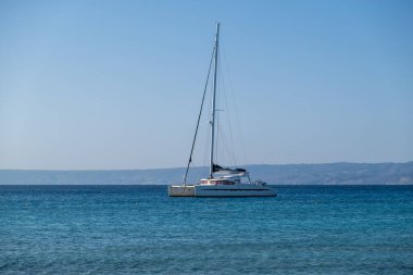 Dalgalanan denize, karaya ve mavi gökyüzüne demirlemiş yelkenli katamaran. Yaz tatili