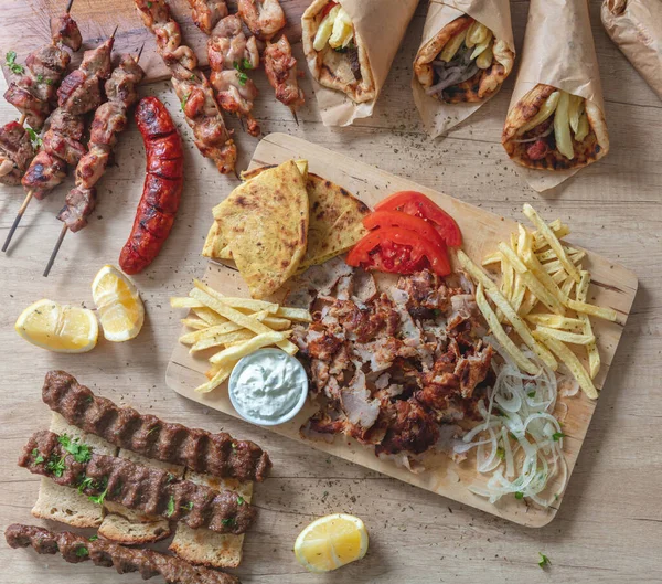 Greek traditional street food, gyro sliced meat, souvlaki, kebab and sausage. Pita bread, tzatziki yogurt, potato tomato and onion on wooden table, top view