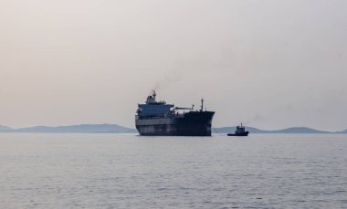 Küçük römorkör, güçlü bir su aracı kargo gemisini Ermoupoli şehir limanı, Syros adası, Cyclades Yunanistan 'a çekiyor. Ege Denizi 'nde Öğleden Sonra