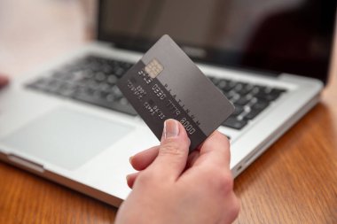 Elleri plastik kredi kartı tutuyor ve dizüstü bilgisayar kullanıyor. Ahşap masa arkaplanı, manzarayı kapatıyor. Çevrimiçi alışveriş kavramı