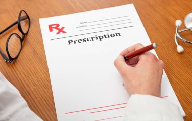 Tıbbi reçete. Kalem tutan kadın doktor, manzaranın üstünde yakın çekim, ahşap ofis masası arka planı. Kadın boş belgeyi teslim eder, boşluğu kopyalar