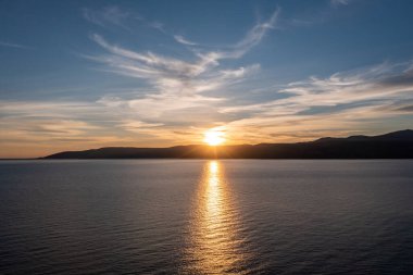 Koufonisia adası üzerinde gün batımı, Kiklad, Yunanistan. Dağ siluetinin üzerinde gün batımı, güneş ışığı altın Ege denizi boyar. Renkli gökyüzü arka planı. 