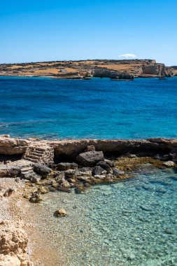 Koufonisia Adası, Cyclades, Yunanistan. Kayalık bir sahile giden taş merdivenler. Sakin Ege Denizi mavisi, turkuaz su, güneşli bir gün açık mavi gökyüzü arkaplanı.