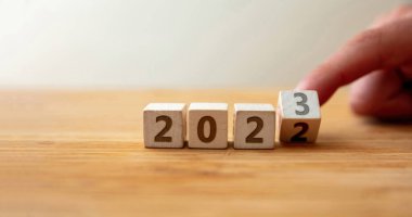 2022 'den 2023' e kadar mutlu yıllar. Ahşap kübün son basamağını çeviren parmak, ahşap masanın üzerindeki yılı değiştiriyor. Yeni plan, iş, kariyer, hedef, başarı.