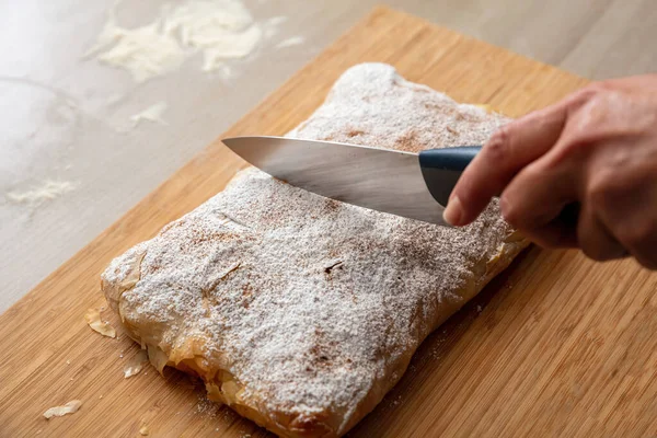 Bougatsa kesen bir bıçakla, tahta bir tahtanın üzerinde geleneksel kremalı turta, yakın görüş. Krema şekeri ve tarçınlı Yunan pastası.