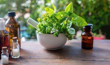 Doğa eczanesi ve homeopati ürünleri. Bitkisel ilaçlar, alternatif şifa. Havanda taze bitkiler ve ahşap masada cam şişeler.