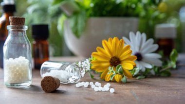 Homeopati eczanesi, bitkisel ilaçlar, doğal ilaçlar. Cam şişeden yayılmış homeopatik küreseller, taze bitki, yeşil doğa arka planı. Alternatif sağlık hizmetleri