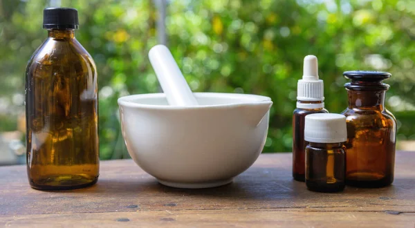 Doğal eczane ve homeopati ürünleri. Beyaz harç ve tokmak ve cam ilaç şişeleri ahşap masa üzerinde, bulanık doğa arka planı