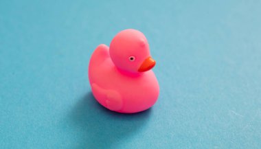 Mavi arka planda izole edilmiş pembe plastik ördek. Bebek banyosu geleneksel oyuncak, lastik ördek yavrusu yüzüyor. Genel Görünüm.
