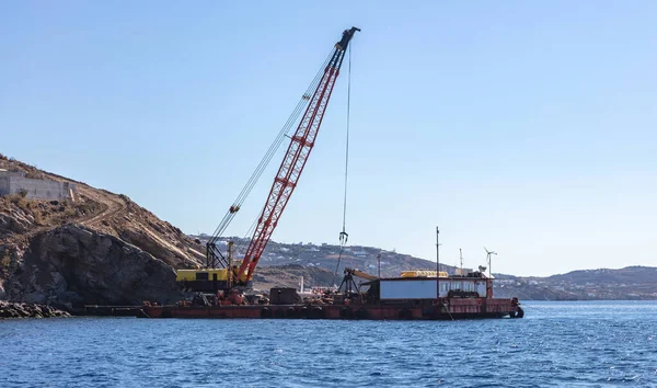 Marine works near Mykonos island port. Cyclades Greece. Construction machine, crane and barge on site, blue sky, rippled Aegean Sea