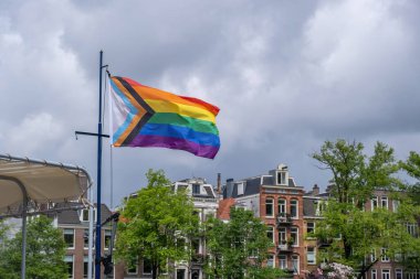 Gay Pride, New Progress LGBTQ gökkuşağı bayrağı rüzgarda dalgalanıyor, Amsterdam şehrinde bulutlu bir arka plan, Hollanda Avrupa