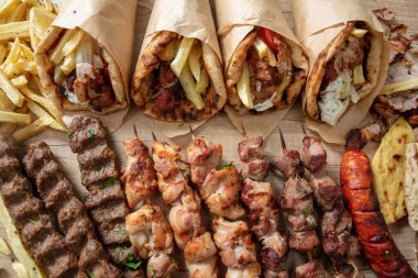 Yunan sokak yiyecekleri, jiroskop dilimlenmiş etli pide dürümü, chiken ve domuz sucuğu şişi. Tahta masa, üst manzara.