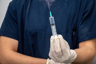 Tıbbi üniformalı doktor, tek kullanımlık eldivenle, şırıngada şırıngayla sıvı uyuşturucuyla el ele tutuşup onu tanıtıyor. Profesyonel doktordan sağlık ve tedavi.