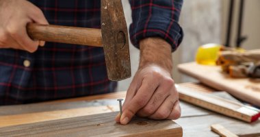 DIY, tamir ve onarım. Marangoz tırnağı. Erkek eli çekiç ve çivi, çalışma masası arka planı.