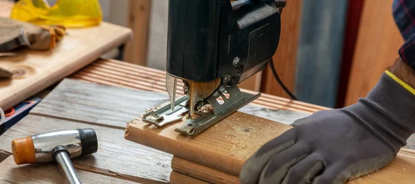 電気時計 大工電動ジグソーで手を切断木材を手袋 建設業界 作業台の閉鎖ビュー — ストック写真