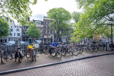 Kanal köprüsüne parketmiş bisikletler. Amsterdam 'ın geleneksel tuğla cepheli evleri. Hollanda 'da güneşli bir gün