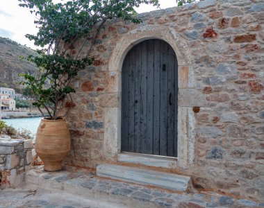 Traditional stonewall building with wooden close door at Mani Laconia, Peloponnese Greece. Ceramic pot, amphora with fresh green plant.  clipart