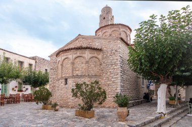 Greece. Areopolis village, Mani Laconia, Peloponnese. Metropolitan temple of Taxiarches, Greek Orthodox stonewall Church at historical square. Traditional cafe, cloudy sky background. clipart