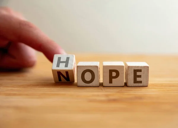 Hope or nope concept. Finger flips letter at wooden cube changing the word nope to hope. Message for modification from pessimism to optimism, negative to positive, gain the success.