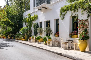 Greek outdoors cafe with empty table and chair on pavement at Kythera Ionian islands Milopotamos village destination Greece. Yellow pots with flowers everywhere