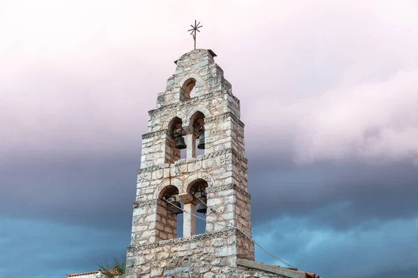 Belfry with four metal bronze bells at Mani Laconia, Peloponnese Greece. Under view of traditional stonewall bell tower with cross, cloudy sky background. Orthodox religious destination.
